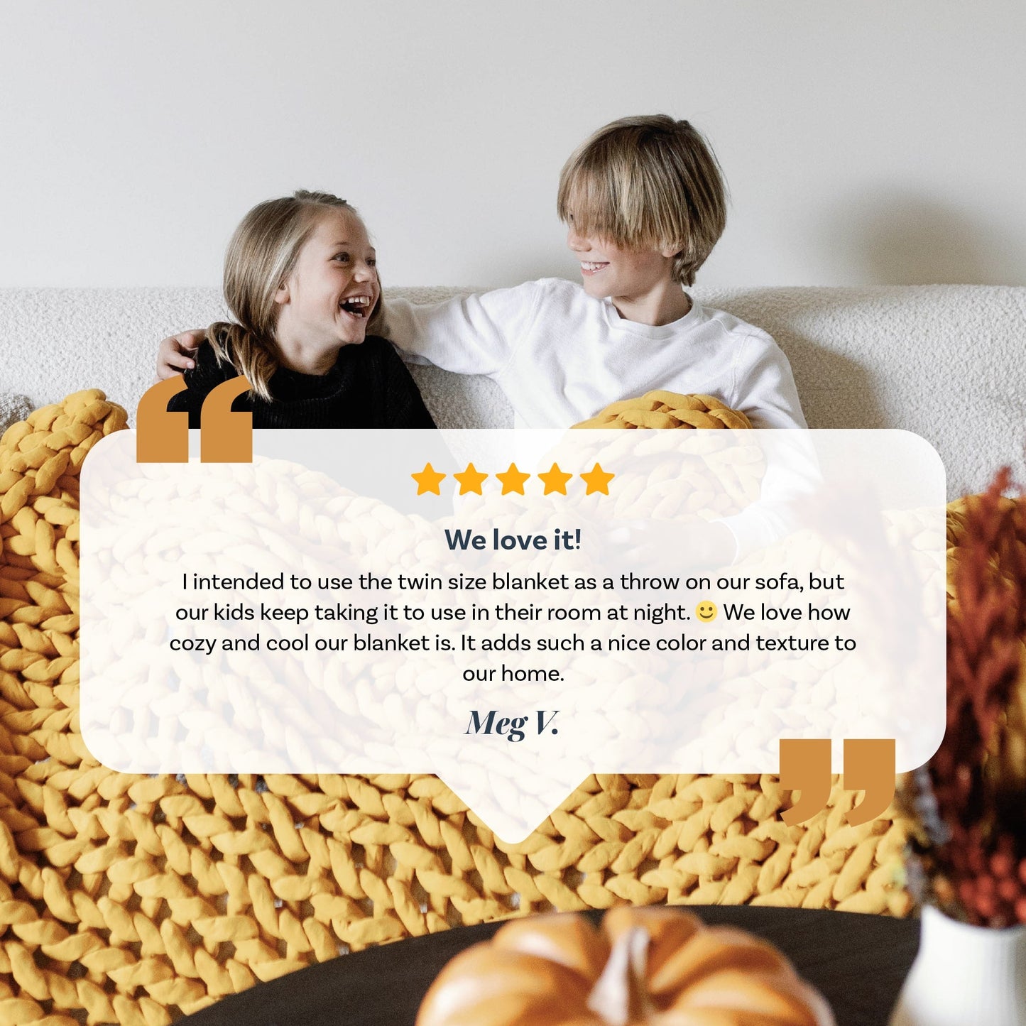 Two smiling children sit on a white couch, cozy under the bright yellow Knit Weighted Blanket. A five-star customer review praising the blanket appears onscreen, with a decorative pumpkin in the foreground.