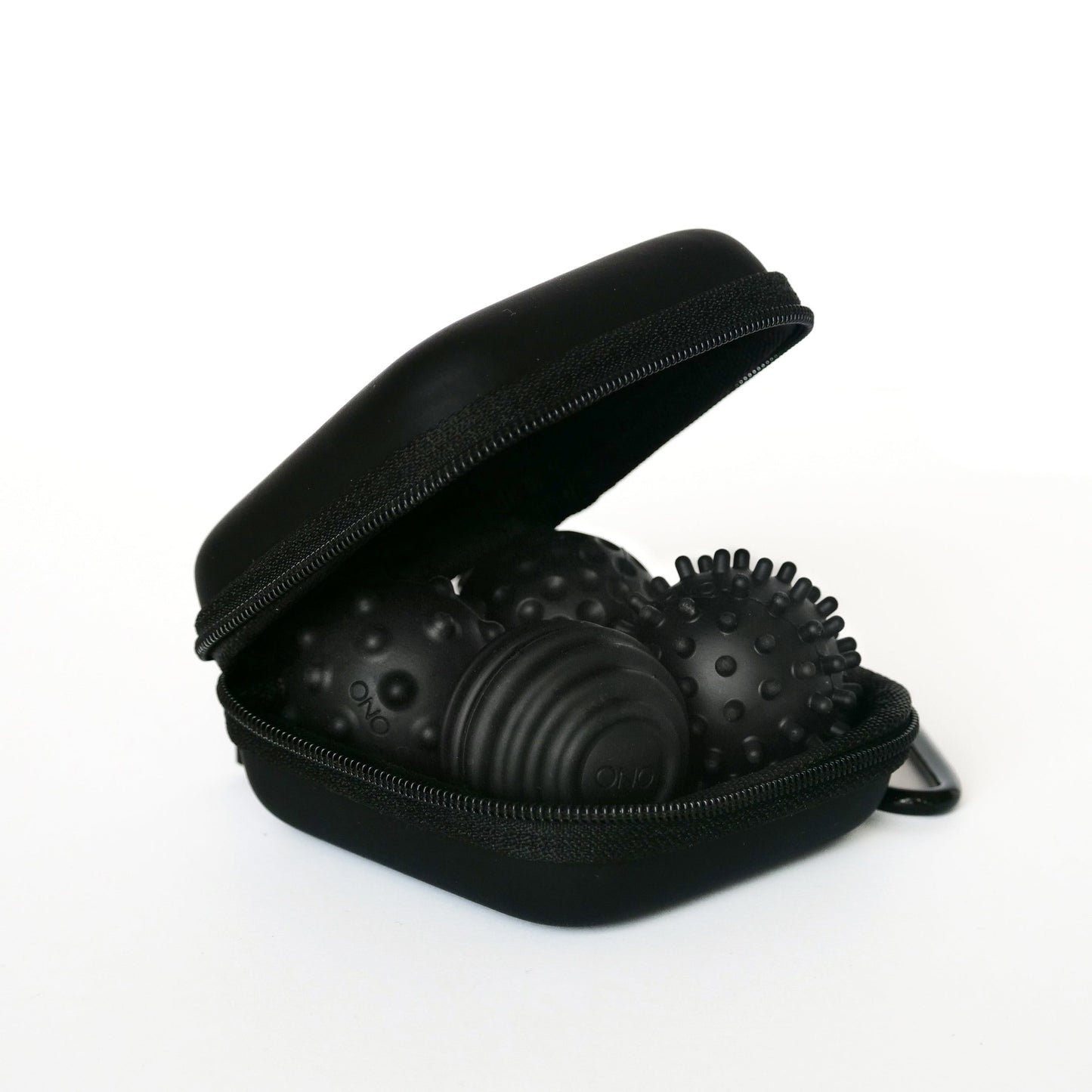 A partially open Onyx Signets case reveals three black textured massage balls with unique surface patterns, perfect for a satisfying fidgeting experience. The background is plain white.
