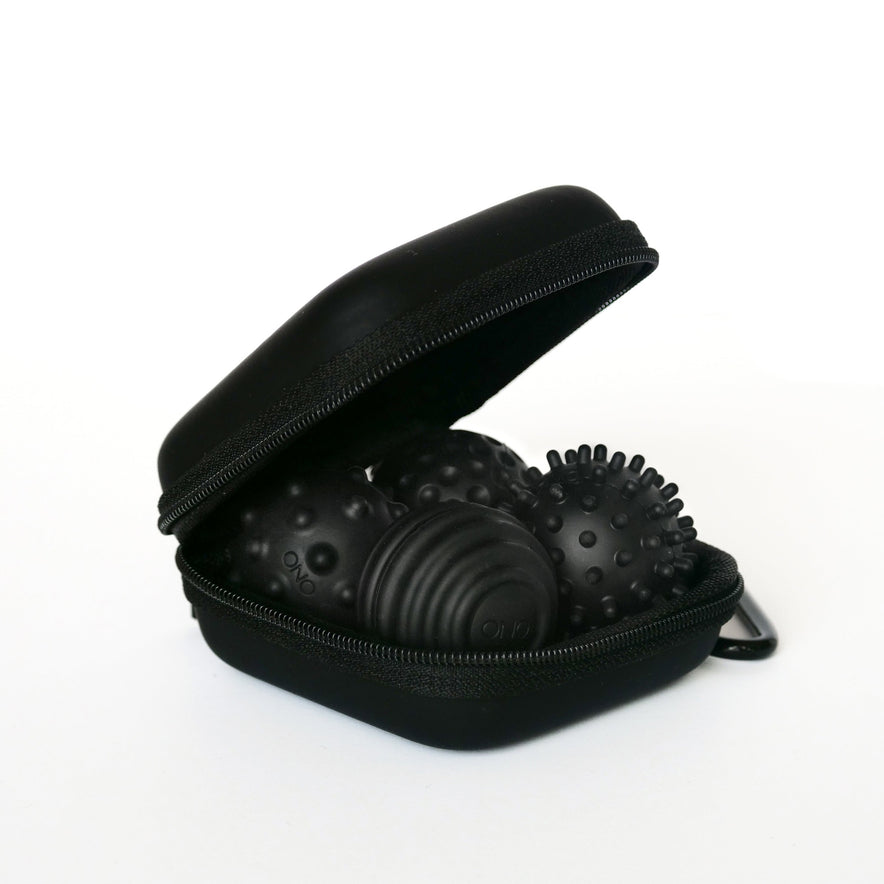 A partially open Onyx Signets case reveals three black textured massage balls with unique surface patterns, perfect for a satisfying fidgeting experience. The background is plain white.