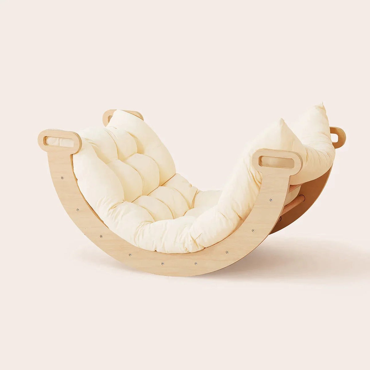 A wooden curved rocker from the 7-in-1 Montessori Climbing Set with Play Pad, featuring a cream-colored tufted padded play cushion compatible with a Pikler triangle.