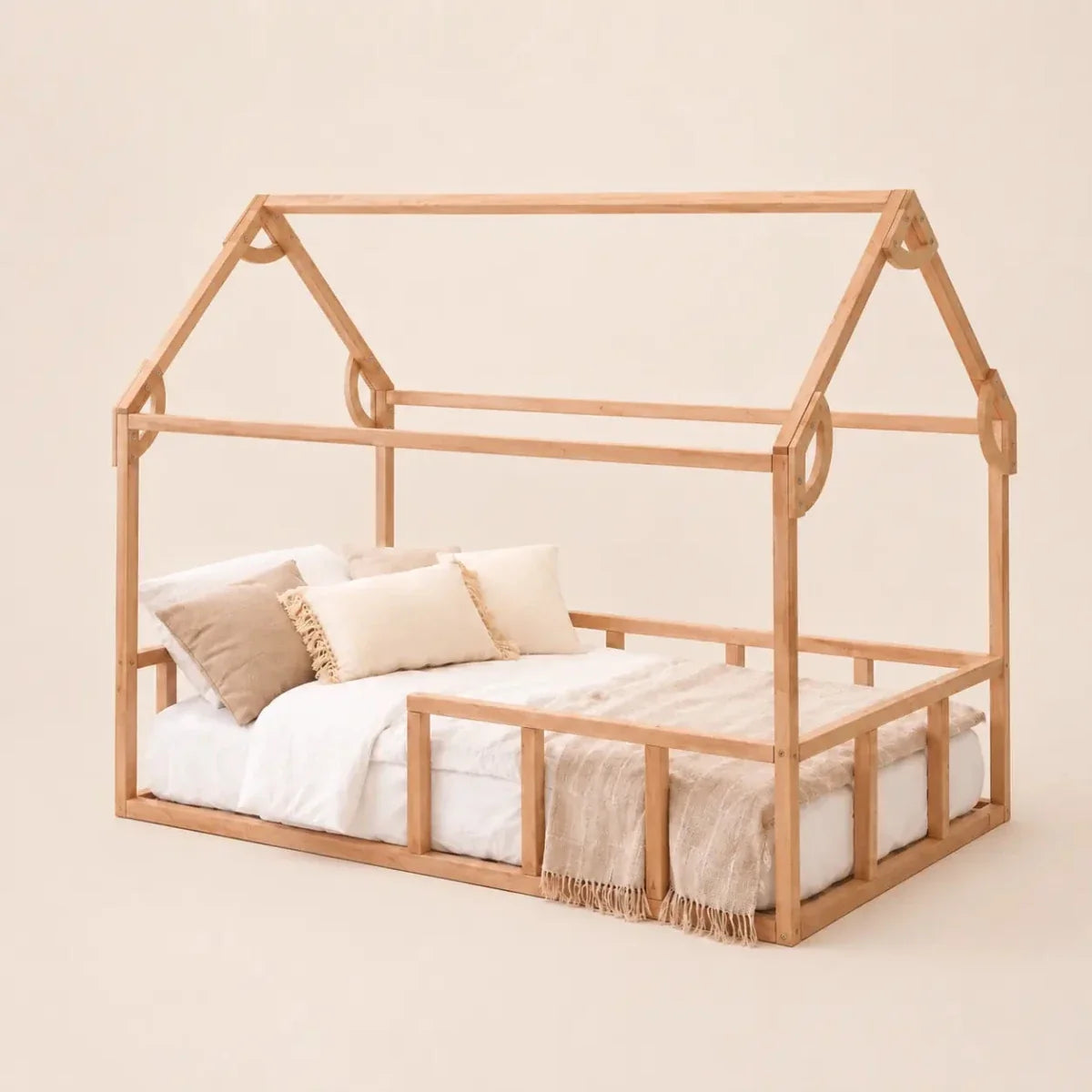 The Twin Size Montessori House Bed for Kids with Fence is crafted from solid beech wood and features a low house-shaped twin bed frame. It comes with a mattress, white and beige bedding, and decorative throw pillows, set against a plain beige background.