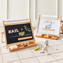 Two oatmeal 3-in-1 Adjustable Tabletop Art easels, one with a blackboard and one with a whiteboard, displaying letters, numbers, and drawings on a patterned rug near a small plush rabbit.