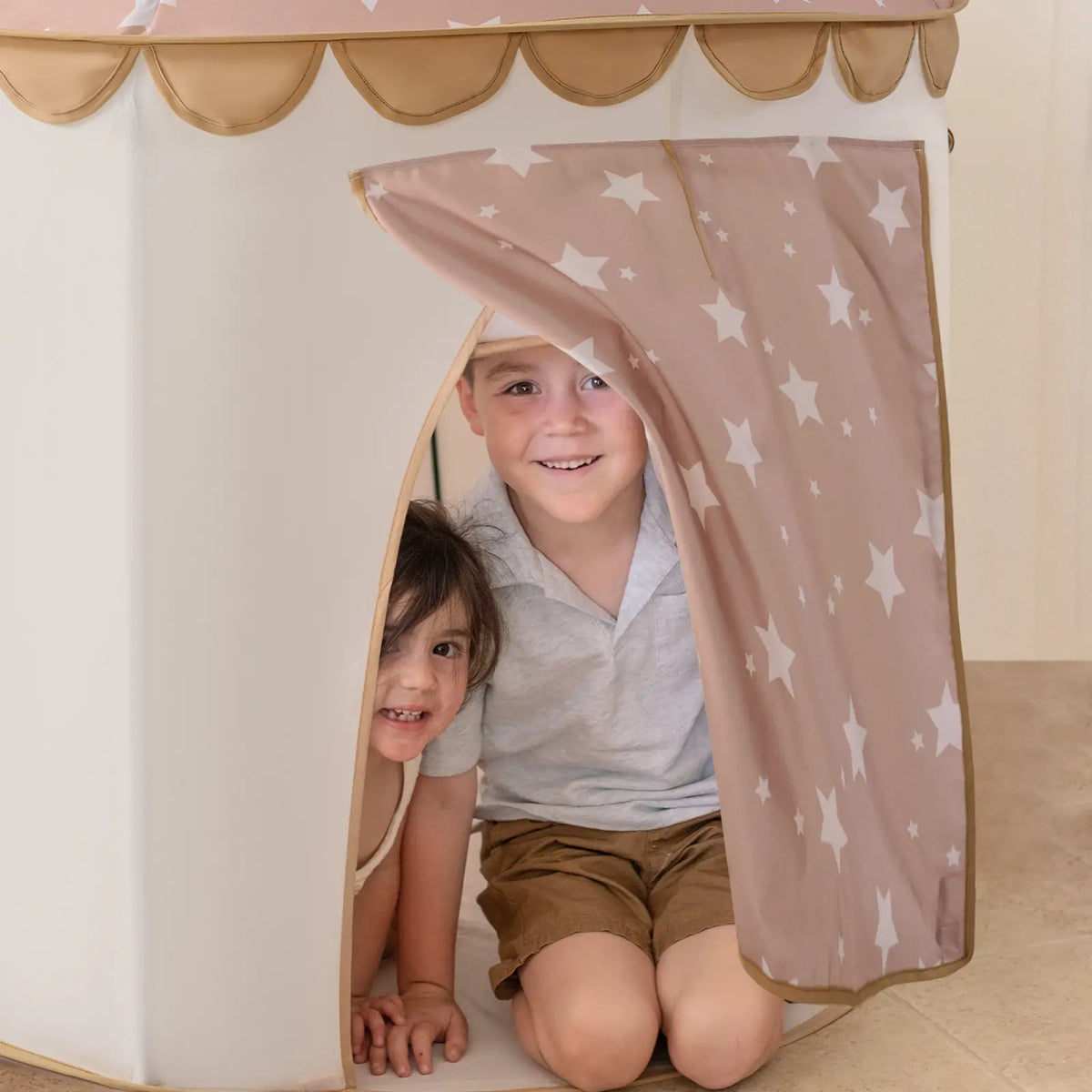 Two children peeking out from inside a Starry Indoor Play Tent for Toddlers.