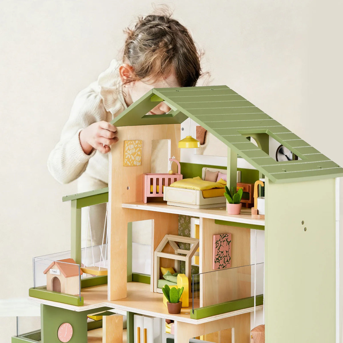 A child interacts with a Sweetwood Cottage Dollhouse (48-pc Furniture) featuring multiple stories and furnished with 1:12 scale miniature beds, plants, and other room accessories.