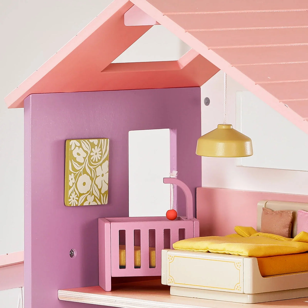 A 1:12 scale Sweetwood Cottage Dollhouse (48-pc Furniture) bedroom featuring a bed, a crib, a yellow pendant light, and a floral wall hanging on the wooden furniture.