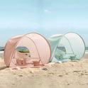 Two pink and light blue Kids Beach Tent & Sand Toy Sets set up on the sand, each containing a small sand toy set inside.