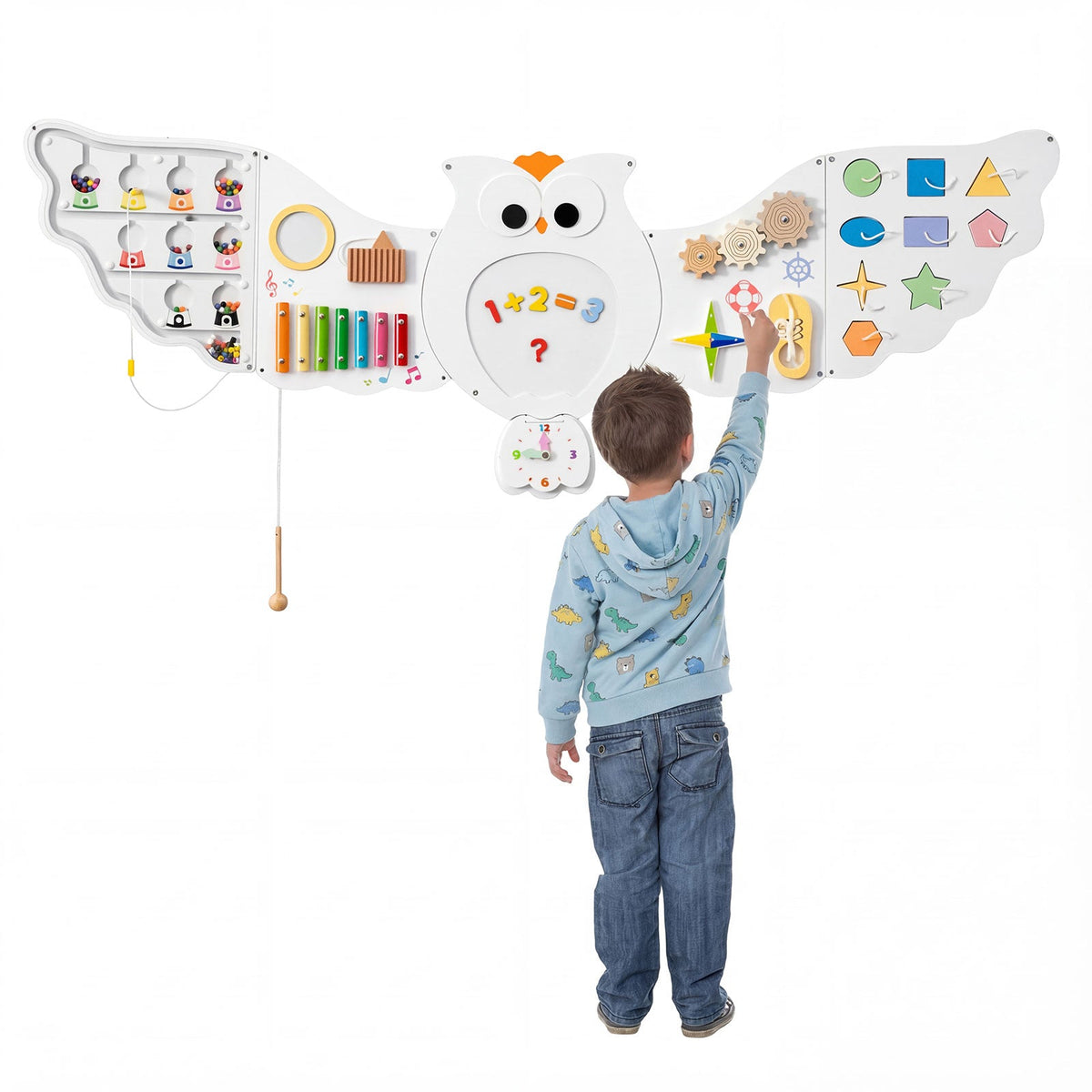 A child stands before an 11-in-1 Owl Wall Busy Board with Magnetic Math, reaching up to touch the colorful magnetic math section on its wing.