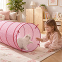 A young girl in pajamas reaches toward a white cat peeking out from a pink and white striped Adventure Crawl Tunnel (68″).