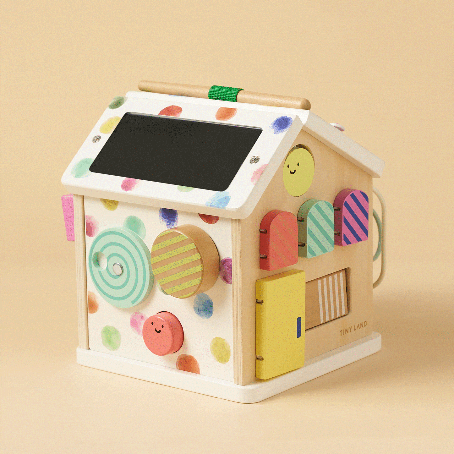 The Montessori Cottage Activity Cube – Rainbow is a house-shaped activity cube decorated with colorful polka dots, featuring interactive components like spinning discs, small doors, and a chalkboard roof to support fine motor skills.