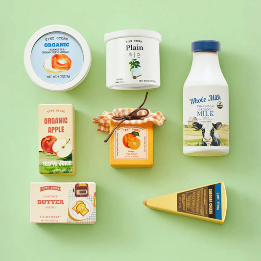 The Pretend Dairy Play Pack includes a tub of cream cheese, a yogurt container, a bottle of milk, a juice box, a jar of fruit spread, a stick of butter, and a wedge of cheddar cheese for a pretend fridge.