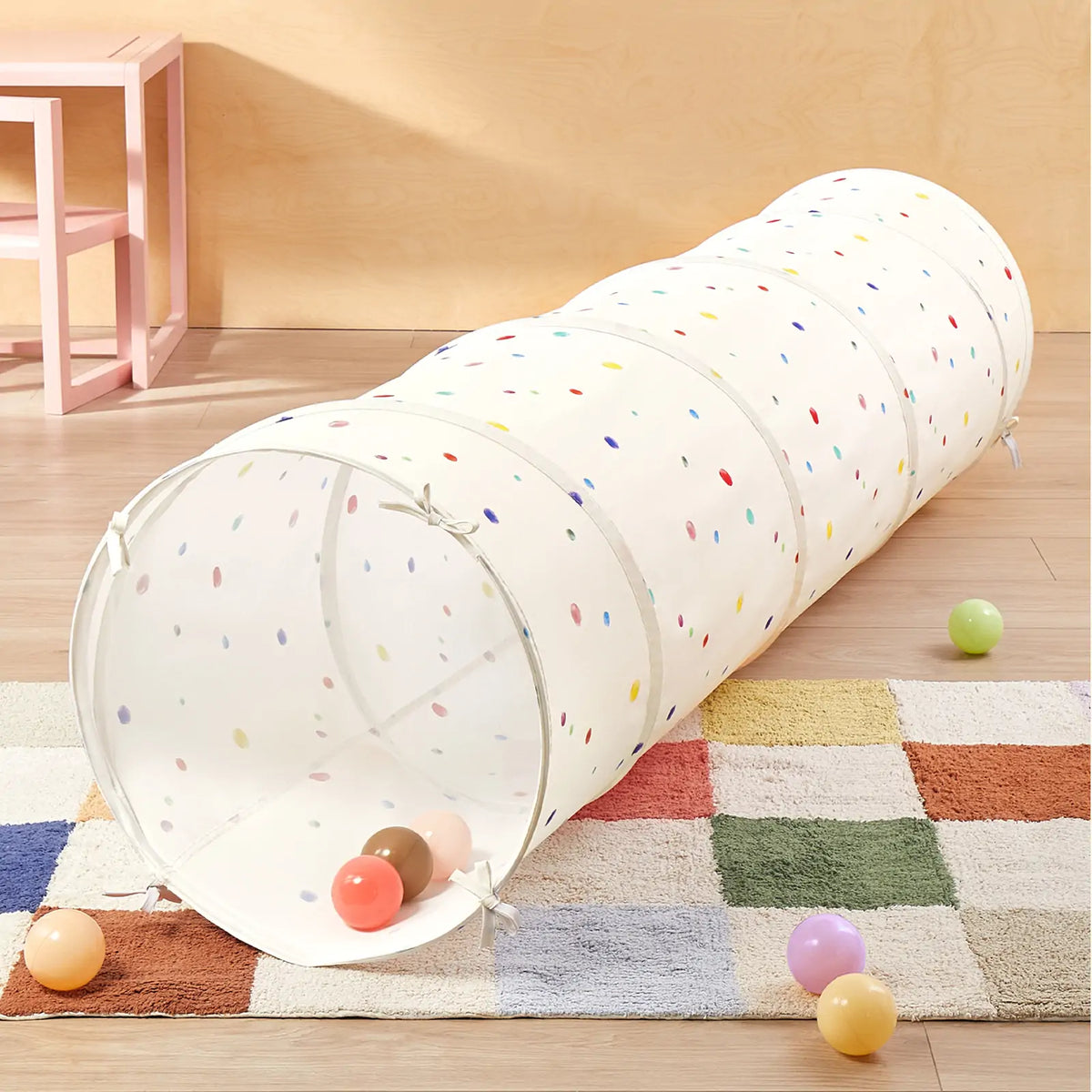 Adventure Crawl Tunnel (68″) in colorful dots, shown as a collapsible fabric tunnel with several small plastic play balls on a multicolored rug.