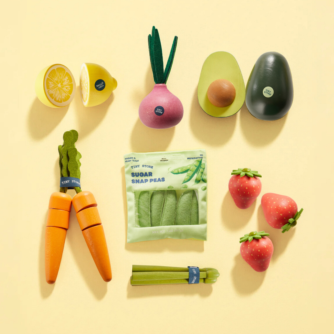 Wooden & Felt Fruit and Veggie Play Pack featuring a sliced lemon, a radish, an avocado, two carrots, a bag of sugar snap peas, three strawberries, and a bunch of celery.