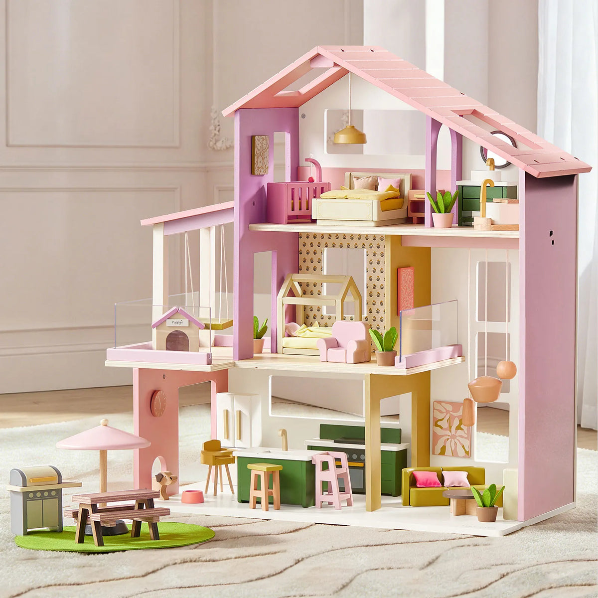A pink 1:12 scale Sweetwood Cottage Dollhouse with three stories of miniature furniture, including a bedroom, kitchen, living room, and an outdoor patio area with a grill and picnic table.