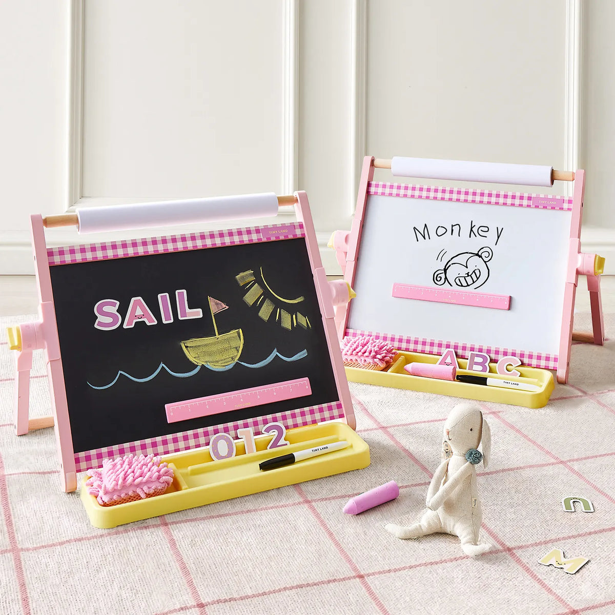 Two pink 3-in-1 Adjustable Tabletop Art Easels, one with a blackboard showing a boat drawing and the word SAIL, and another with a whiteboard showing a monkey drawing and the word Monkey.