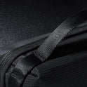 Close-up of the black Tech Pouch with textured fabric and a strong woven strap, displayed on a dark, reflective surface. The image showcases detailed stitching and high-quality materials, emphasizing its role as a travel organizer.