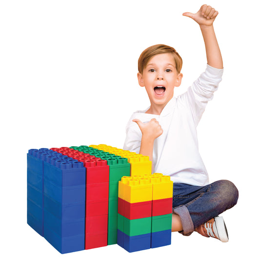 A smiling child sits on the floor, giving a thumbs up and pointing to colorful Jumbo Building Blocks 48 PC - Learner Set in blue, red, green, and yellow stacked beside them.