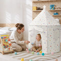 A toddler sits inside a white, dotted Starry Indoor Play Tent for Toddlers, playing with plastic balls alongside a woman, with an activity walker nearby on a round rug.