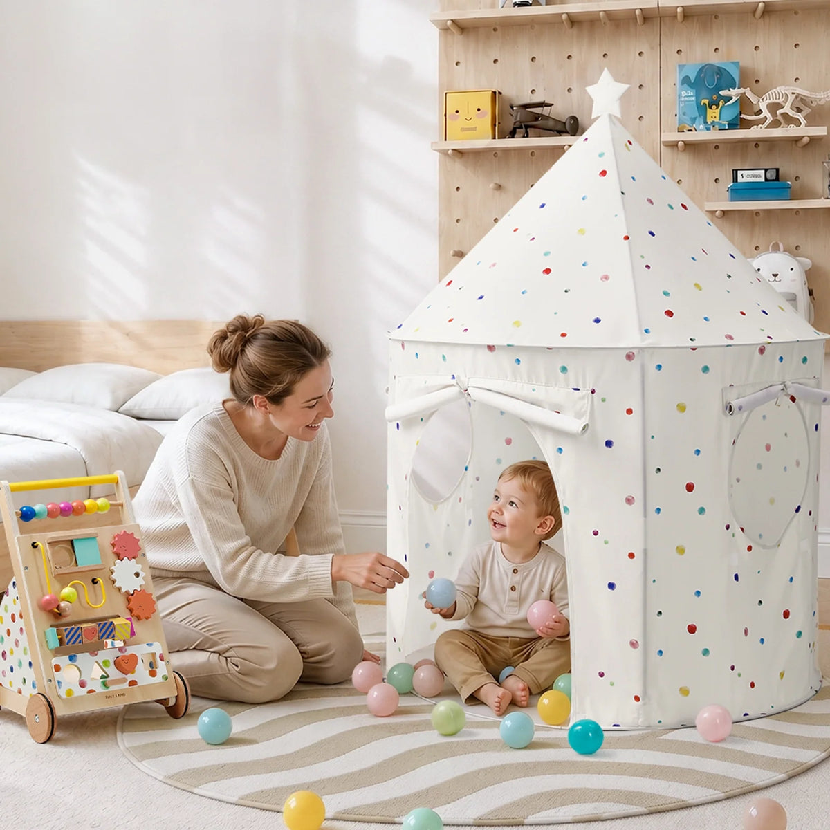 A toddler sits inside a white, dotted Starry Indoor Play Tent for Toddlers, playing with plastic balls alongside a woman, with an activity walker nearby on a round rug.