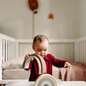A toddler in a maroon dress stacks a 10 pc Silicone Rainbow Stacking Toy on a white table.