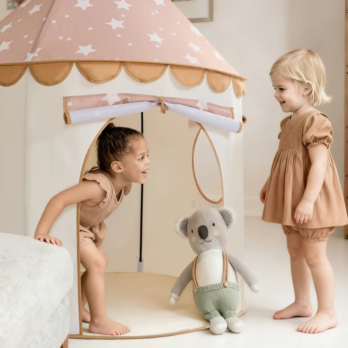 Two toddlers play with a koala stuffed animal inside and outside a conical, star-patterned Starry Indoor Play Tent for Toddlers.