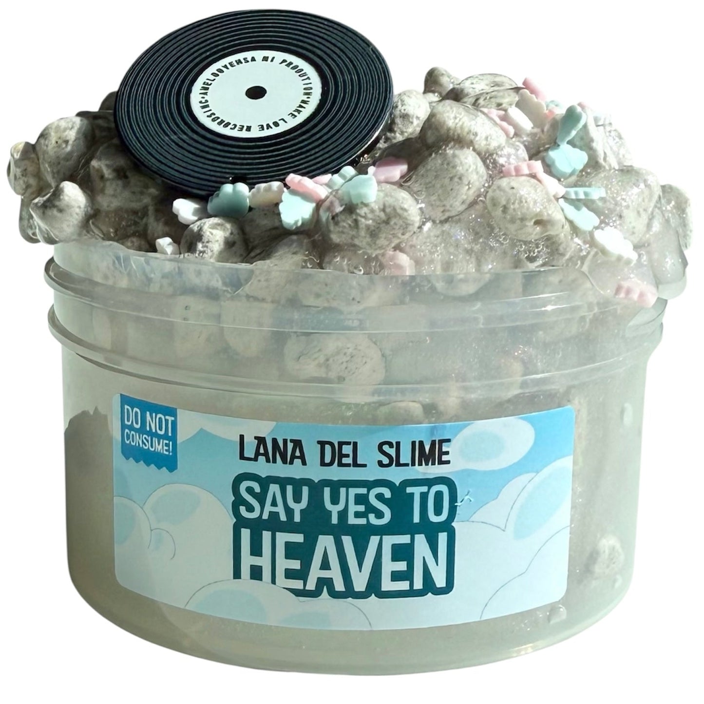 A clear 7 oz container labeled "Say Yes To Heaven Pumice Slime With Cloud Sprinkles And Record Charm" features fluffy gray, Pepsi Cola-scented exfoliating slime with pastel sprinkles, a vinyl record charm, and a “Do not consume!” sticker.