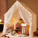 A Large Cozy Cabin Play Tent with Star Lights featuring sheer curtains, a toy kitchen, a stuffed mouse, and alphabet blocks on the floor.
