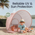 A child sits inside a pink, dome-shaped Kids Beach Tent & Sand Toy Set surrounded by toys, with text reading Reliable UV & Sun Protection and a UPF 50+ UV Protection badge.