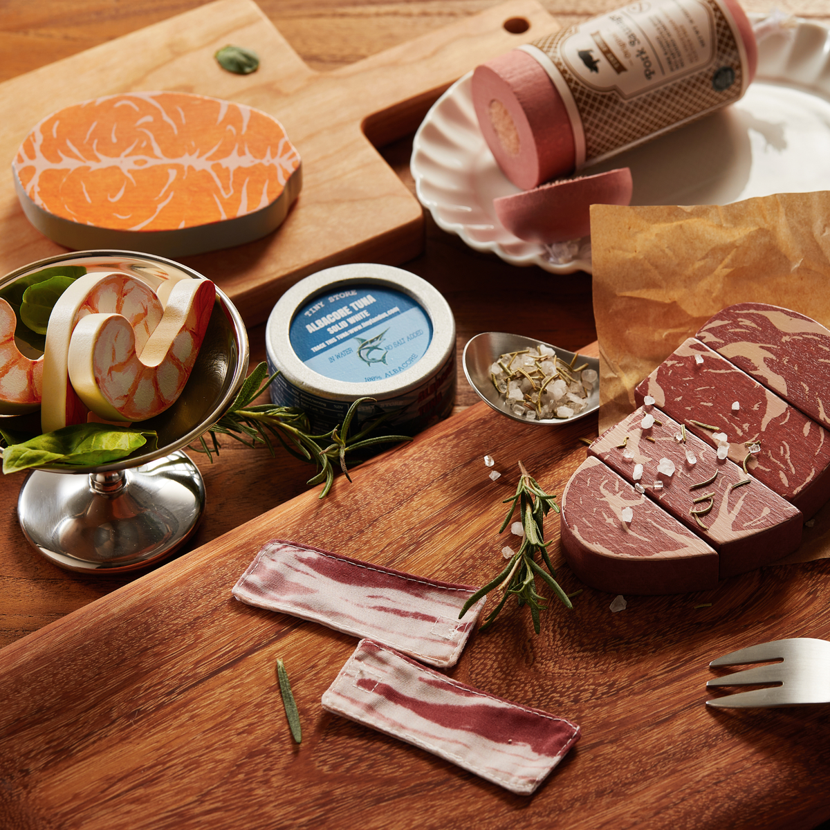 Pretend Meat & Seafood Play Pack including a salmon fillet, shrimp in a bowl, a tuna can, a sausage log, bacon strips, and sliced steaks on wooden cutting boards for a pretend grill.