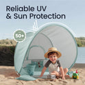 A toddler wearing a sun hat sits inside a Kids Beach Tent & Sand Toy Set with a bucket, toy train, and truck; text reads Reliable UV & Sun Protection with a UPF 50+ badge on the UV-protective fabric.