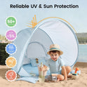 A child sits in a light blue gingham Kids Beach Tent & Sand Toy Set on the sand, holding a toy shovel next to a sand toy set, with icons showing UV, wind, and water protection features.