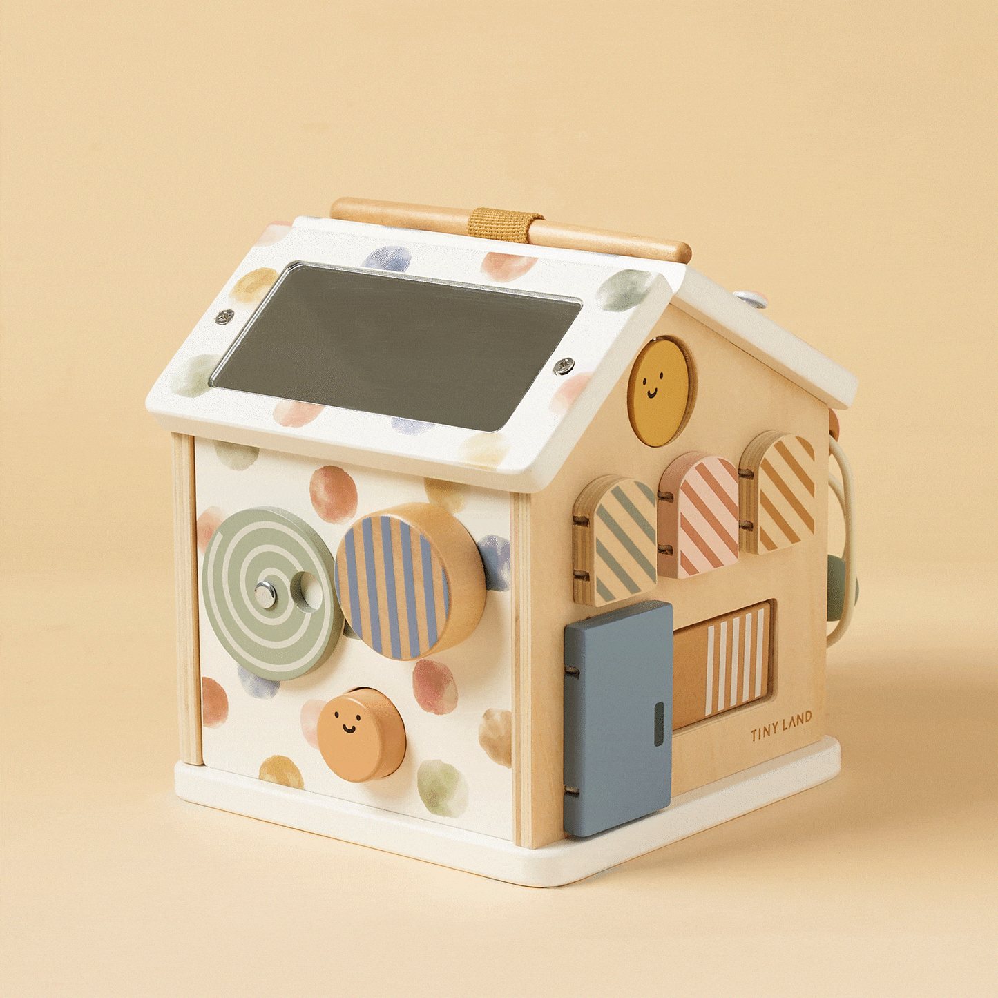 The Montessori Cottage Activity Cube – Morandi is a wooden house-shaped toy featuring a mirror on the roof, spinning discs, and small doors with colorful patterned accents to encourage fine motor skills.