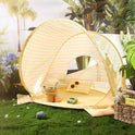 A yellow and white striped Kids Beach Tent & Sand Toy Set on grass, containing a bucket, a sand toy set, and sunglasses.