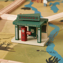 A wooden toy service station with a red gas pump from the 1920s Railway Wooden Train Table with Sounds sits on a printed map play mat, creating a charming vintage city scene.