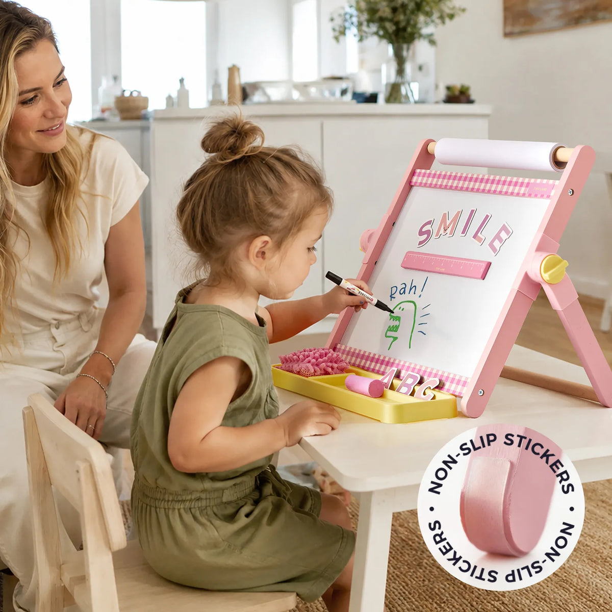 A young girl draws on a pink 3-in-1 Adjustable Tabletop Art Easel while an adult watches, with an inset circle showing a close-up of a non-slip sticker on the leg of the adjustable kids easel.