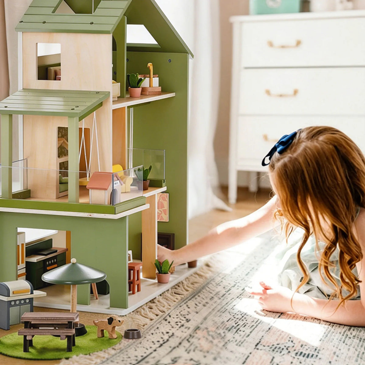 A child playing with a three-story Sweetwood Cottage Dollhouse furnished with miniature 1:12 scale furniture and accessories.
