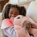 A smiling child shares a calming hug with a Mylo the Moon Pal – 5 lb Weighted Plush, a large, ultra-soft pink weighted toy.