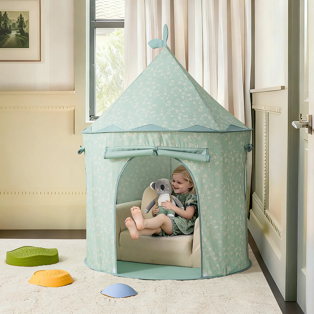 A toddler sits inside a light green conical Starry Indoor Play Tent for Toddlers, holding a koala plush toy.