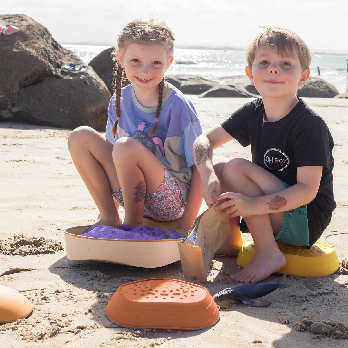 A girl and a boy sit on the beach playing with Stacking Balance Stepping Stones – Sunset, a colorful plastic balance course of stacking stones.