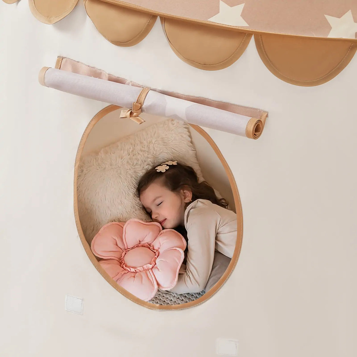 A young girl sleeps inside a Starry Indoor Play Tent for Toddlers, resting her head on a flower-shaped pillow near an oval window.
