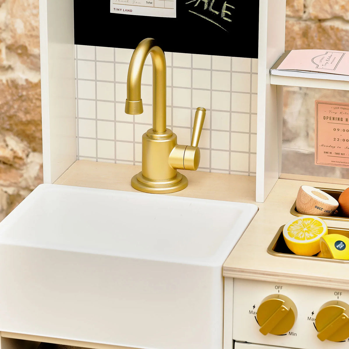 BistroSwitch 2-in-1 Play Kitchen & Bistro featuring a toy sink with a gold faucet, a tiled backsplash, and toy fruit on the counter for immersive role-play.
