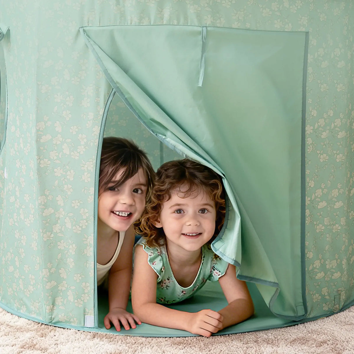 Two smiling children peeking out from the opening of a floral-patterned Starry Indoor Play Tent for Toddlers.