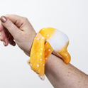 An orange, star-patterned Ori Mini Wrist Hugger – Magnetic Sensory Plush wraps comfortably around a person’s wrist.