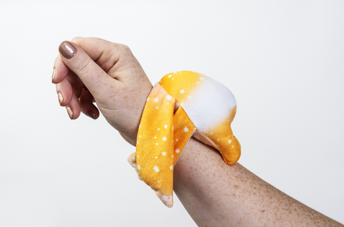 An orange, star-patterned Ori Mini Wrist Hugger – Magnetic Sensory Plush wraps comfortably around a person’s wrist.