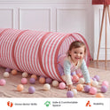 A toddler crawls out of a pink and white striped Adventure Crawl Tunnel (68″) surrounded by colorful plastic balls.