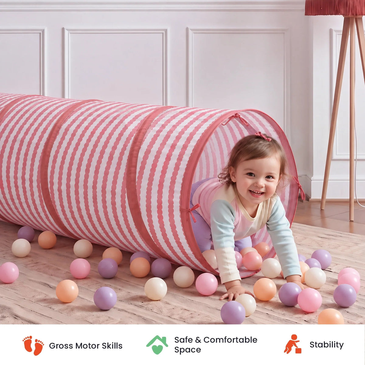 A toddler crawls out of a pink and white striped Adventure Crawl Tunnel (68″) surrounded by colorful plastic balls.