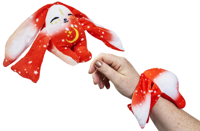 A Rover Mini Wrist Hugger – Magnetic Sensory Plush red rabbit toy with a yellow crescent moon and stars, shown both flying and as a magnetic wrist toy.