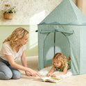 A woman kneels on the floor pointing to a book for a young child lying inside a pale green floral Starry Indoor Play Tent for Toddlers.