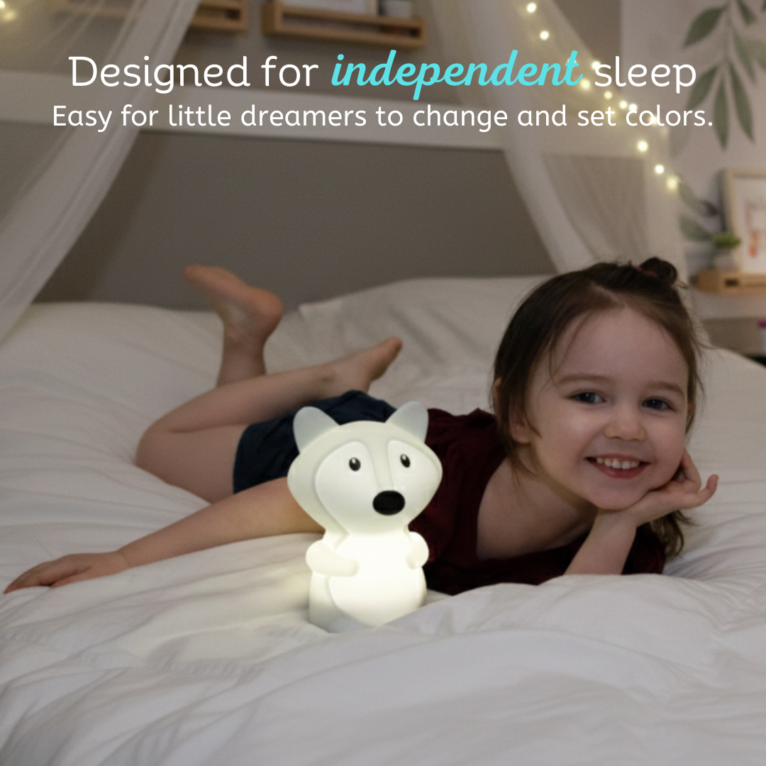 A smiling child lies on a bed next to a Felix the Fox Mini Night Light, an illuminated fox-shaped lamp, with text above reading: Designed for independent sleep. Easy for little dreamers to change colors and learn their hues.