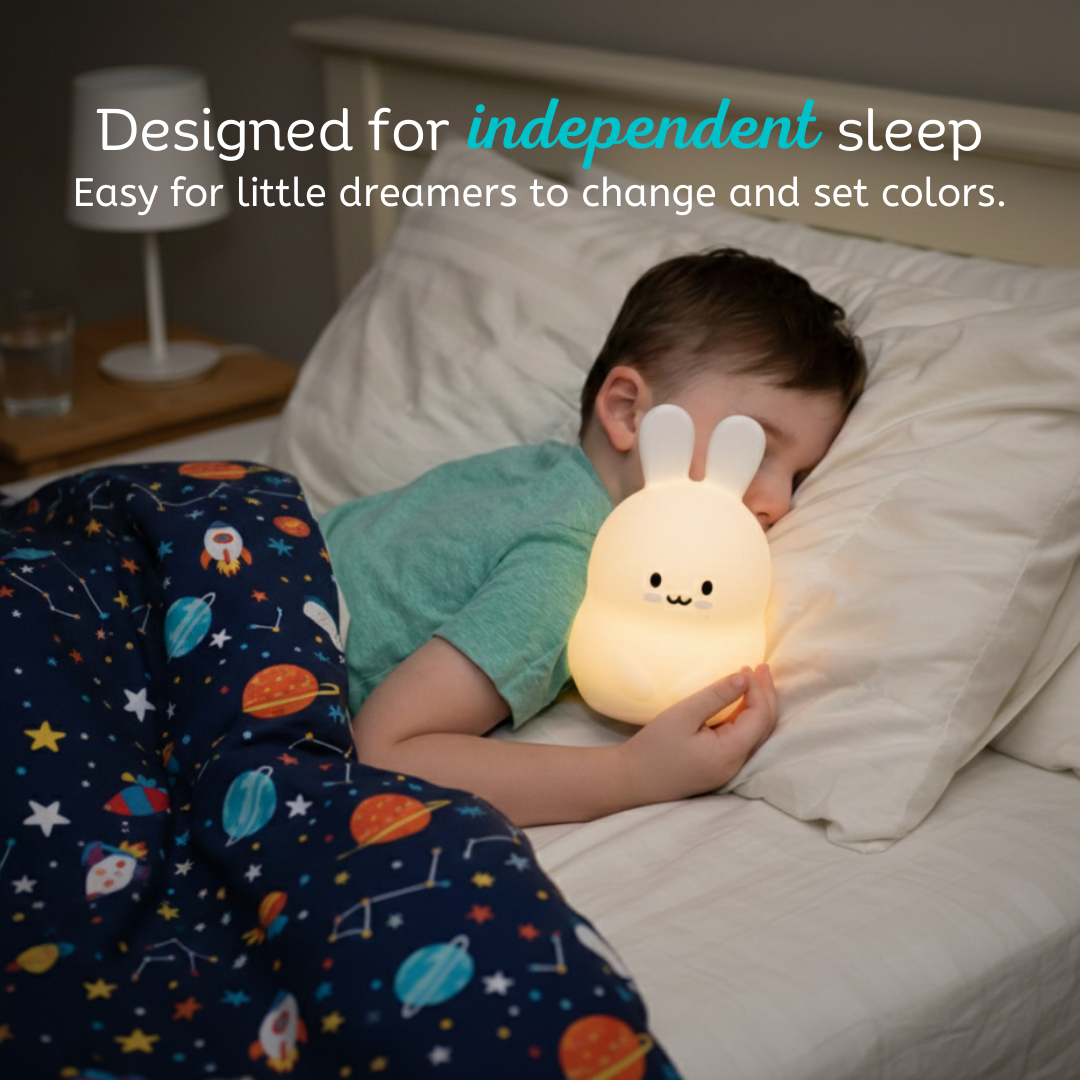 A child sleeps in bed while holding a glowing Baxter the Bunny Silicone Night Light, with text above reading, Designed for independent sleep. Easy for little dreamers to change and set colors.
