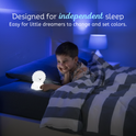 A child lies in bed smiling as they touch a Luther the Lion Silicone Night Light, a color-changing, rechargeable lion-shaped silicone lamp designed to help little dreamers independently change and set colors.